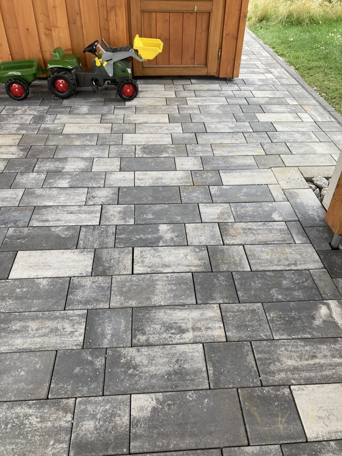 Fertig gepflasterte Hoffläche mit Carport in dunklem Betonpflaster